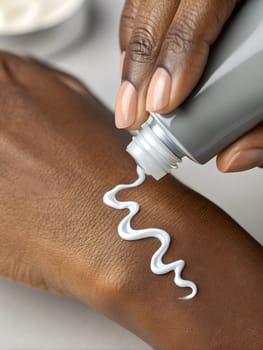 Beautiful dark-skinned woman's hand applying cream on skin. Close-up in light background. Skin care concept, moisturizing or nourishing cream. High quality photo