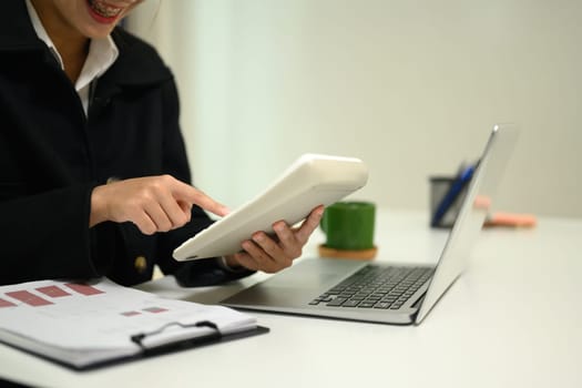 Female accountant using calculator and reviewing reports with charts and transaction details.