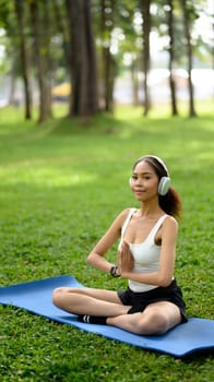 Serene young African woman wearing headphones practicing yoga on mat in a park.