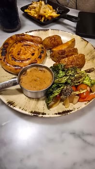 mouthwatering German worst curled up cumberland sausage meal featuring a grilled sausage, loaded cheese fries, and fresh vegetables served on a rustic plate. Perfect for dinner lovers appreciating hearty and flavorful dishes.