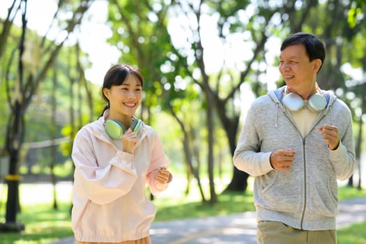 Cheerful father and daughter jogging on a sunny park path. Health and family activity concept.