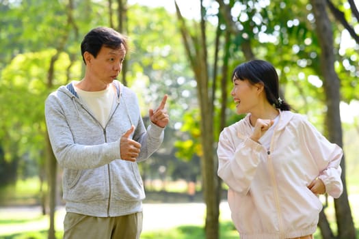Cheerful father and adult daughter in a lively conversation while exercising together in a park.
