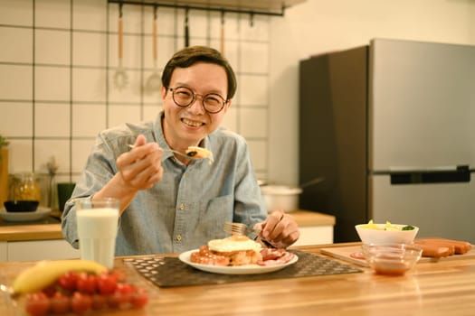 Middle aged man enjoying a hearty breakfast on wooden table in cozy home kitchen.