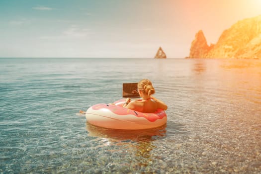 Woman laptop sea. Freelancer woman in sunglases floating on an inflatable big pink donut with a laptop in the sea. People summer vacation rest lifestyle concept