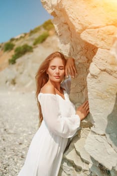 A woman in a white dress is standing on a rocky beach. Concept of serenity and tranquility, as the woman is enjoying the natural beauty of the beach