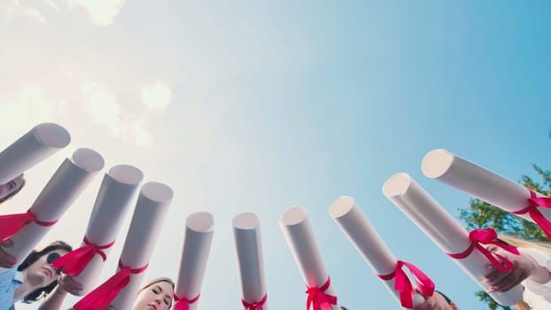 Graduates join their diplomas in a circle against the sky