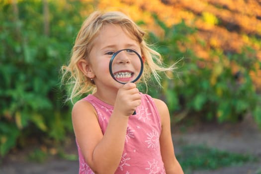 A child looks through a magnifying glass in nature. Selective focus. Kid.
