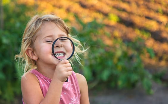 A child looks through a magnifying glass in nature. Selective focus. Kid.
