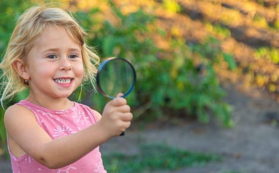 A child looks through a magnifying glass in nature. Selective focus. Kid.