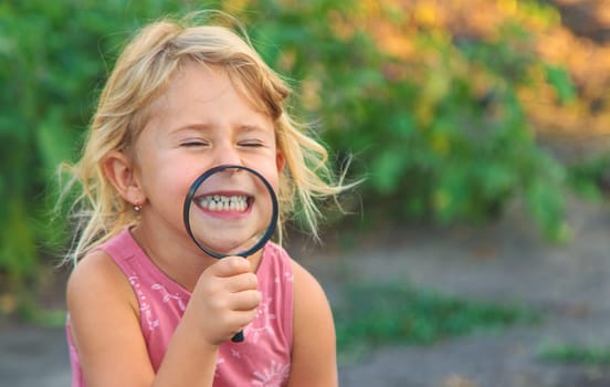 A child looks through a magnifying glass in nature. Selective focus. Kid.