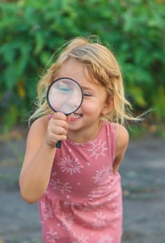 A child looks through a magnifying glass in nature. Selective focus. Kid.