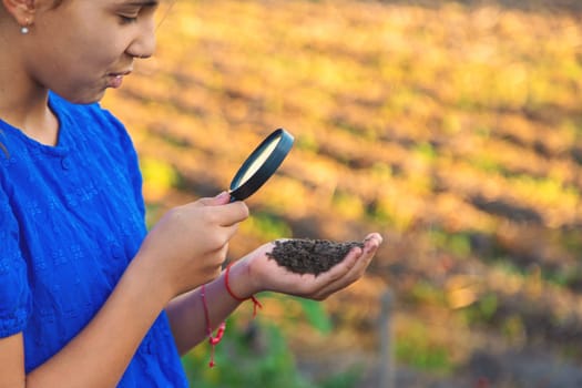 A child looks at the soil through a magnifying glass. Selective focus. Kid.