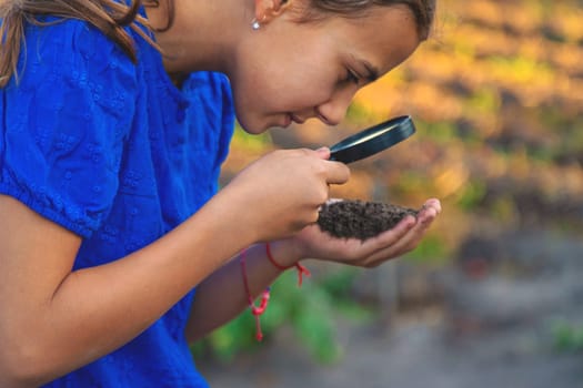 A child looks at the soil through a magnifying glass. Selective focus. Kid.