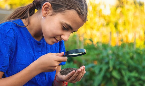 A child looks at the soil through a magnifying glass. Selective focus. Kid.