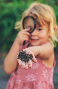 A child looks at the soil through a magnifying glass. Selective focus. Kid.