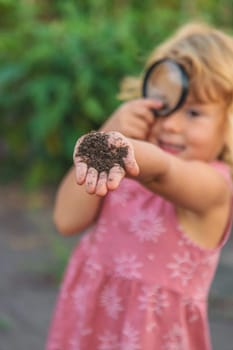 A child looks at the soil through a magnifying glass. Selective focus. Kid.