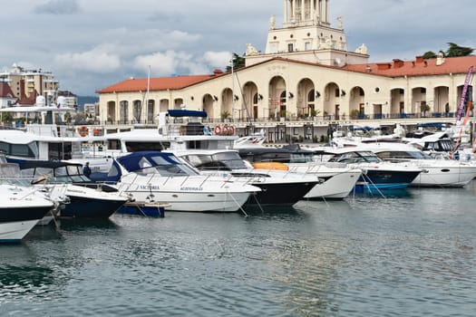 Yachts and boats docked at a marina next to a historic building in a coastal city under a cloudy sky in the late afternoon - Sochi, Russia April 14, 2023.