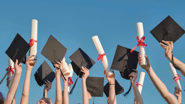 Group of students celebrating their graduation by throwing their hats and diplomas in the air