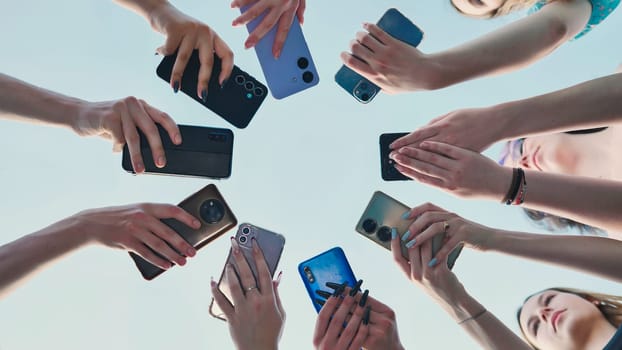 Group of friends holding smartphones making a circle with mobile phones in the sky