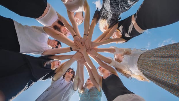 Group of young women is joining hands in a circle outdoors, showing their unity and teamwork.