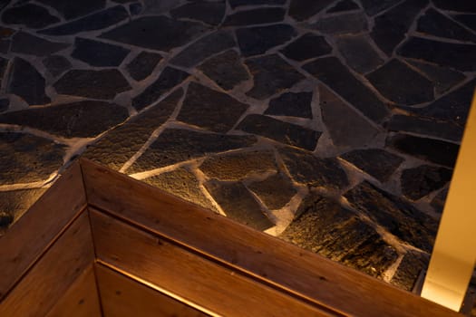 A closeup view showcases a beautifully textured stone floor, featuring wooden corners and lit with warm lighting