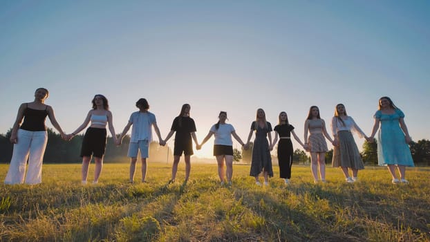 Group of friends are holding hands in a field at sunset, celebrating their graduation from school