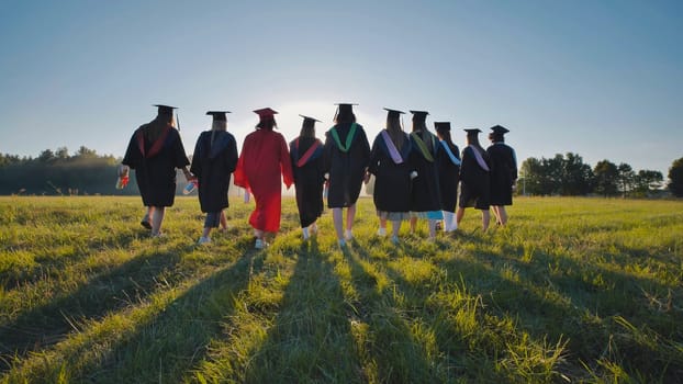 Six graduates in robes walk against the backdrop of the sunset.