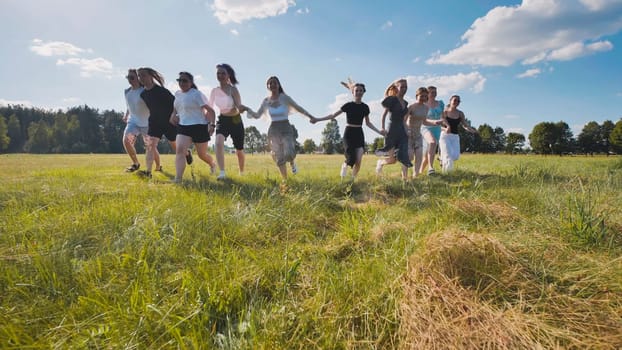Group of friends is running through a field, holding hands and celebrating their graduation