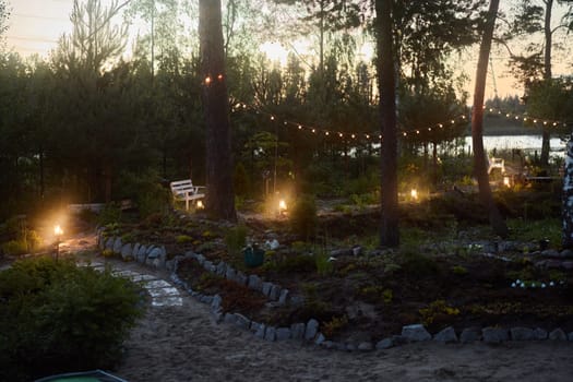 A tranquil and serene garden at dusk, beautifully adorned with gentle lights and surrounded by trees near the water