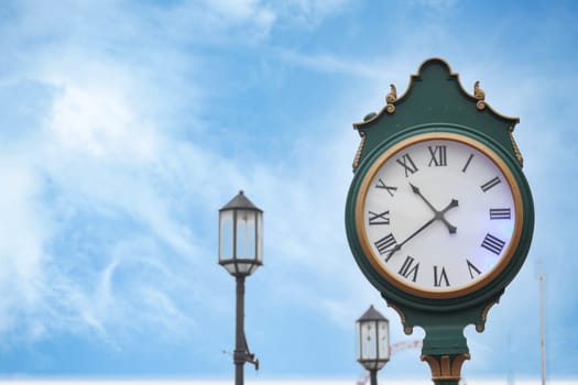 A vintage street clock elegantly placed near lampposts against a beautiful blue sky backdrop