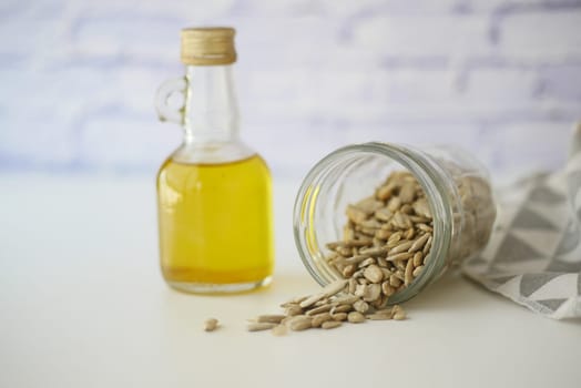 A bottle of sunflower oil is placed next to a glass jar that has spilled seeds inside it