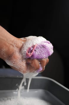 A hand firmly squeezing a soapy sponge, resulting in the creation of bubbles and foam