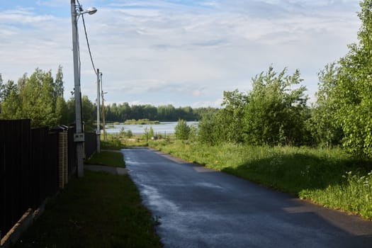 A tranquil pathway winds to a serene waterway, surrounded by lush greenery, vibrant bushes, and tall trees