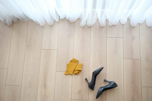Stylish black heels and a vibrant yellow scarf are beautifully displayed on a wooden floor