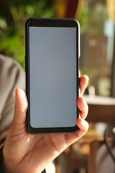 A closeup image of an individual holding a smartphone, which features a completely blank screen