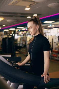 A young woman with a ponytail exercises on a treadmill in a bright, modern gym filled with fitness equipment. The atmosphere is energetic and motivating, showcasing a health-focused environment.