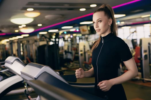 A woman exercises on a treadmill in a well-equipped gym, surrounded by various fitness machines and bright lights. She focuses on her workout, determined to stay fit and healthy.