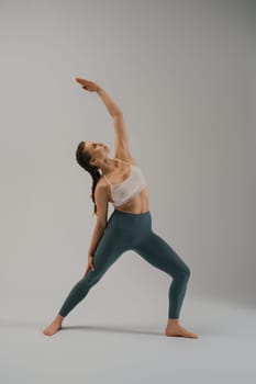 A fit woman demonstrates a yoga pose in a minimalist studio. Her focus and grace highlight the serenity of the moment, showcasing both physical strength and mental balance.