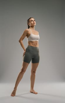 A fitness model stands confidently in a studio, showcasing her toned physique and athletic wear. The soft lighting accentuates her strength and posture, creating an inspiring atmosphere.