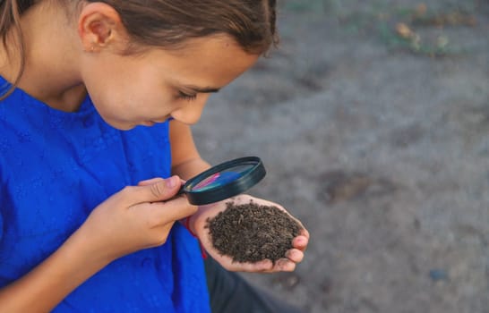 A child looks at the soil through a magnifying glass. Selective focus. Kid.