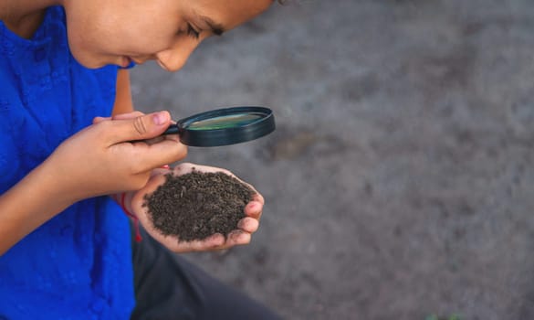 A child looks at the soil through a magnifying glass. Selective focus. Kid.
