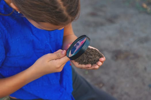A child looks at the soil through a magnifying glass. Selective focus. Kid.