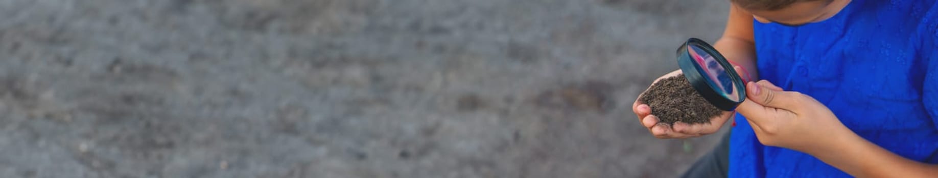 A child looks at the soil through a magnifying glass. Selective focus. Kid.