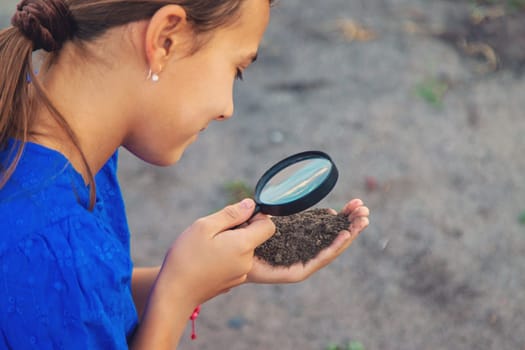 A child looks at the soil through a magnifying glass. Selective focus. Kid.
