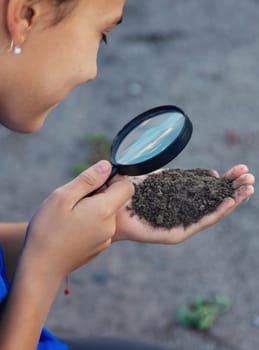 A child looks at the soil through a magnifying glass. Selective focus. Kid.