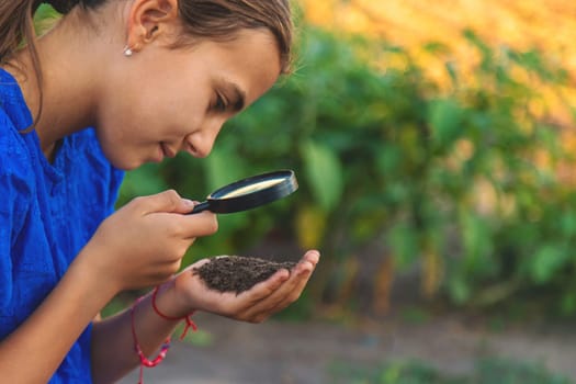 A child looks at the soil through a magnifying glass. Selective focus. Kid.