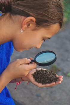 A child looks at the soil through a magnifying glass. Selective focus. Kid.