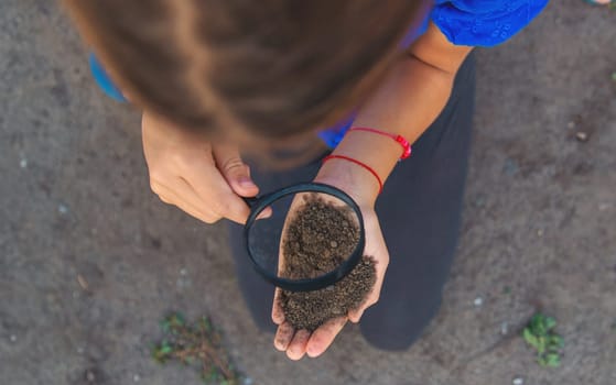 A child looks at the soil through a magnifying glass. Selective focus. Kid.