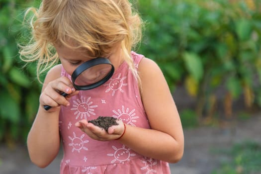 A child looks at the soil through a magnifying glass. Selective focus. Kid.