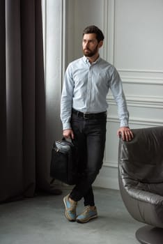 A fashionable man stands with a bag in a contemporary room, embodying urban style and professionalism.